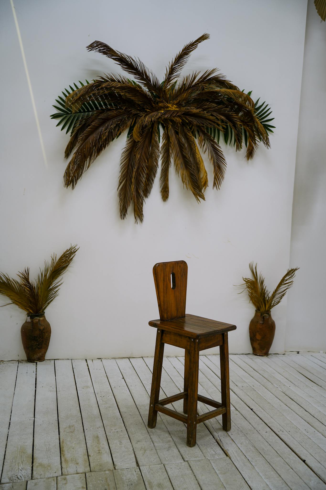 A minimalist indoor space featuring a wooden chair and dried palm decor for a rustic vibe.